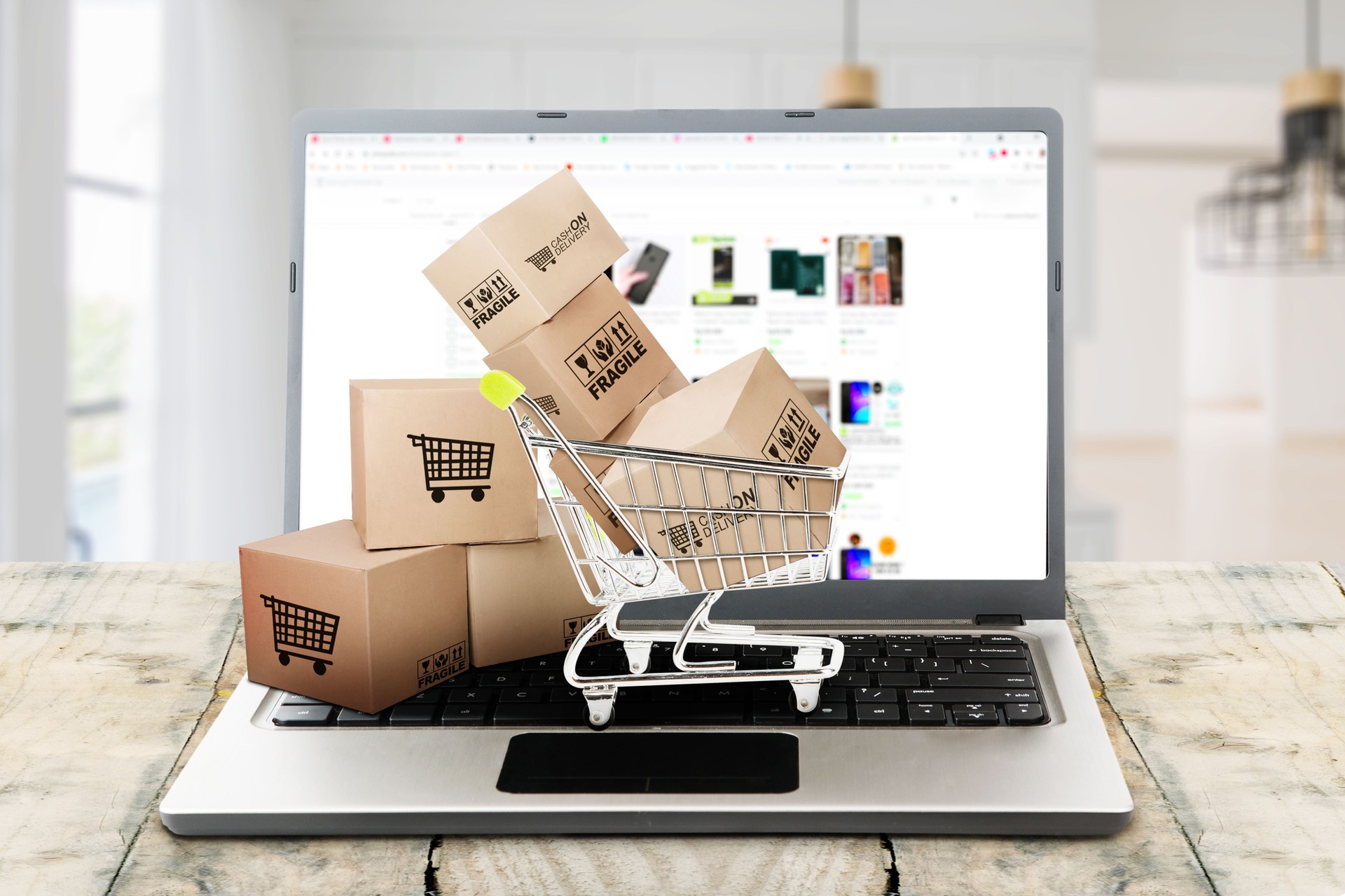 Laptop mit geöffnetem Online-Shop, davor kleine Versandkartons und ein Mini-Einkaufswagen – symbolisiert den Aufbau eines modernen, klar strukturierten Online-Shops für kleine Unternehmen und Handwerksbetriebe.